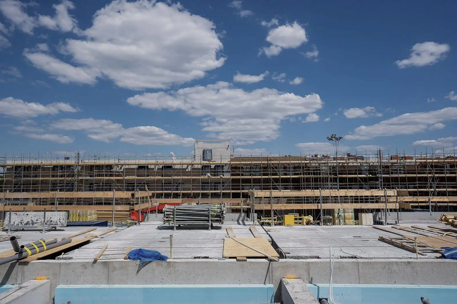 Canteiro de obra de grande extensão com estrutura de concreto, andaimes e materiais organizados