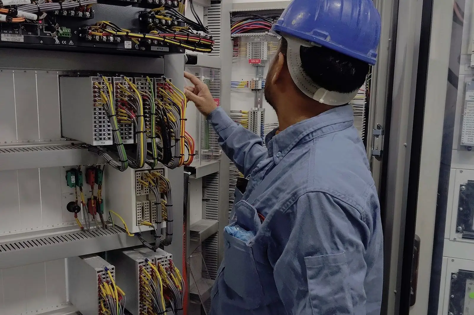 Profissional com capacete inspecionando um painel elétrico industrial com cabos organizados