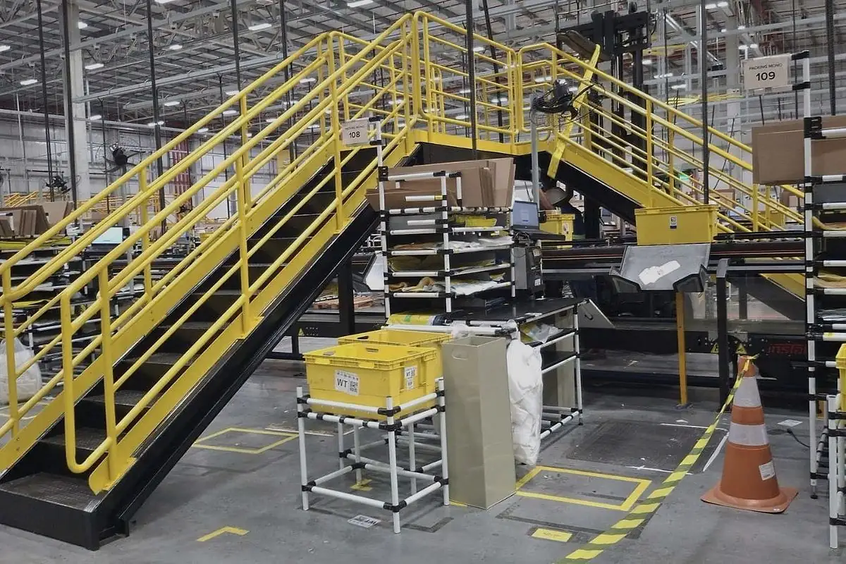 Escada e plataforma de acesso com guarda-corpo instaladas entre estações de trabalho de um centro de distribuição