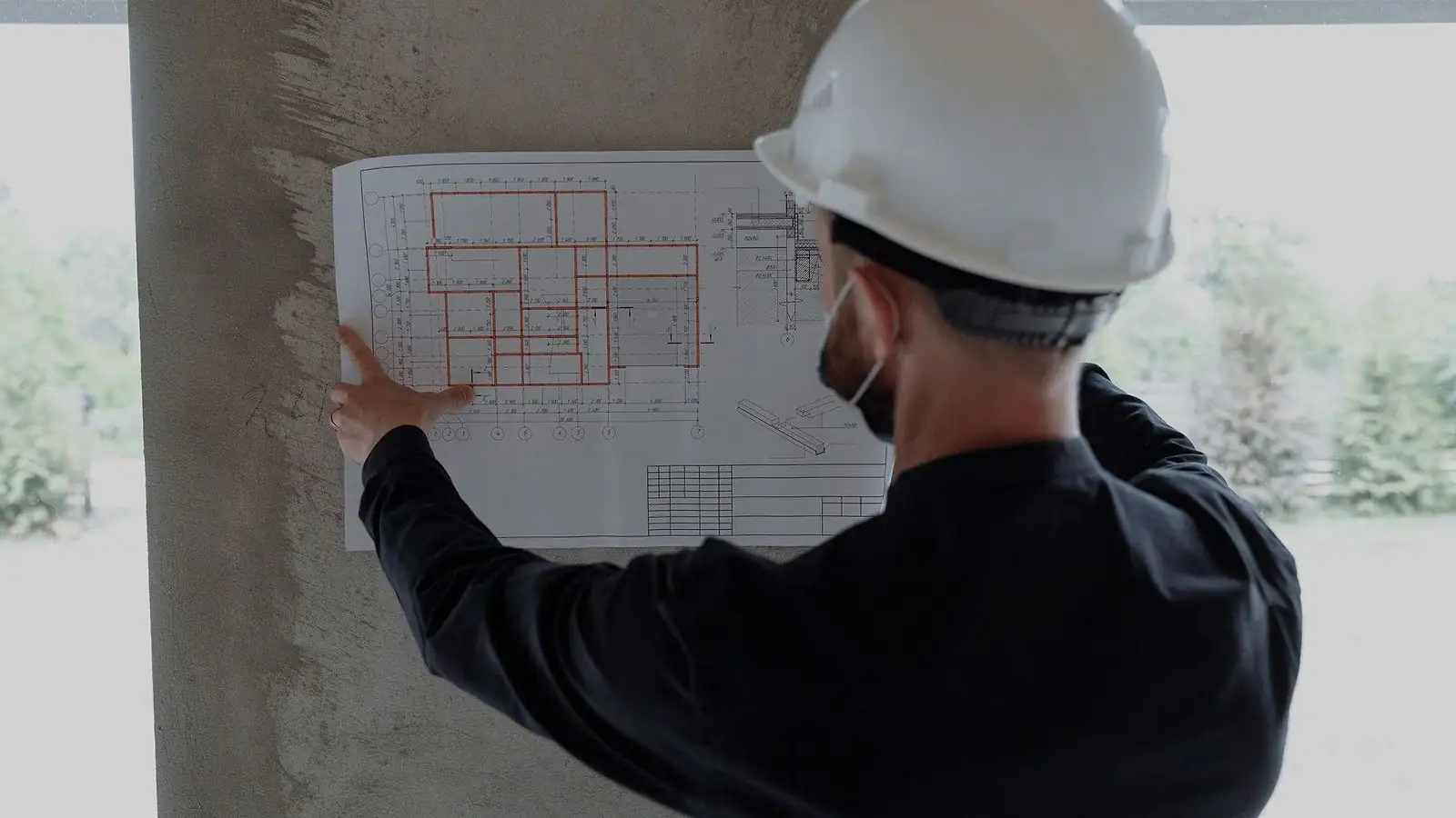 Profissional de capacete conferindo prancha de projeto apoiada em pilar de concreto