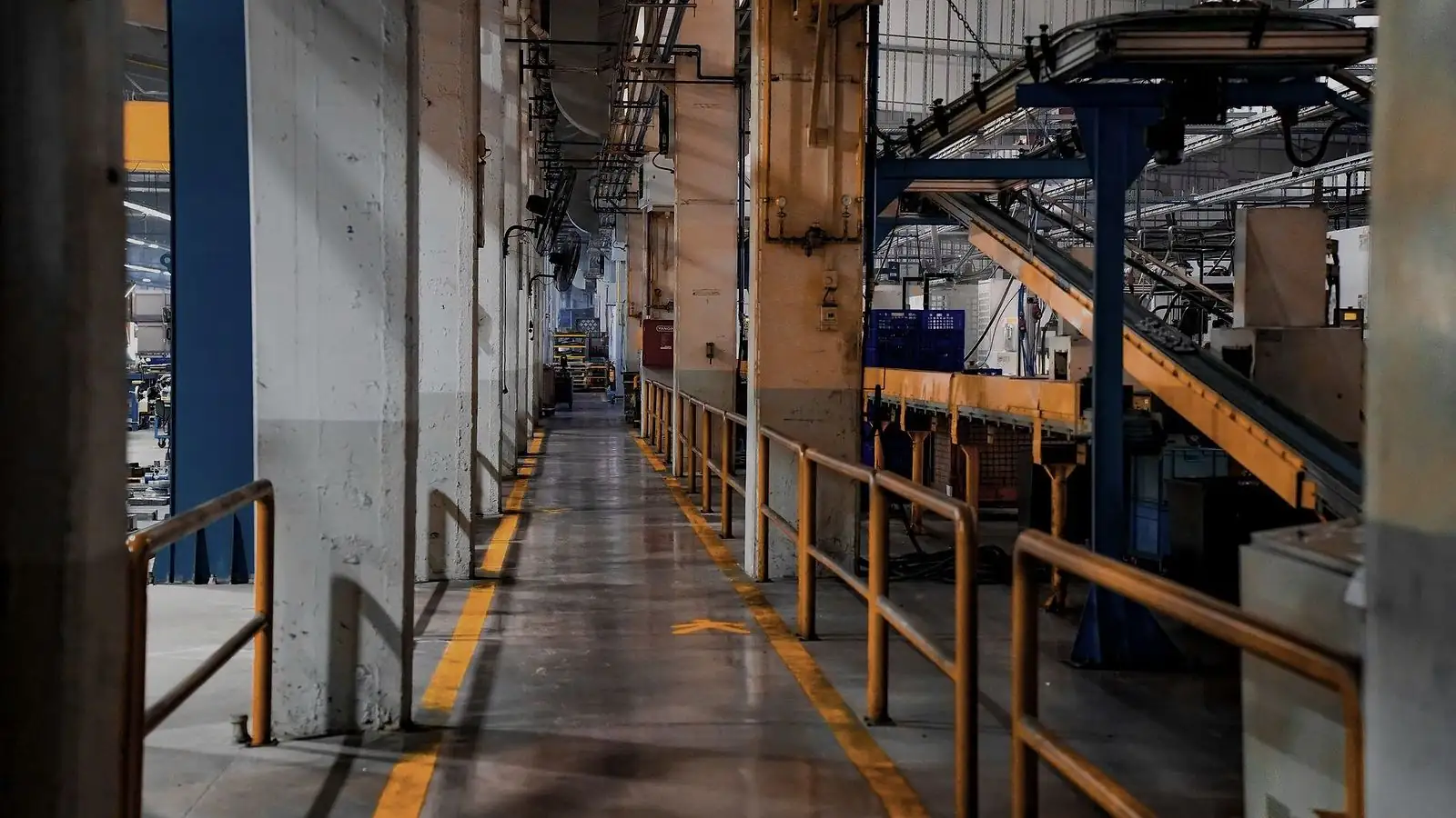 Corredor de circulação demarcado entre linhas de produção e esteiras em planta industrial
